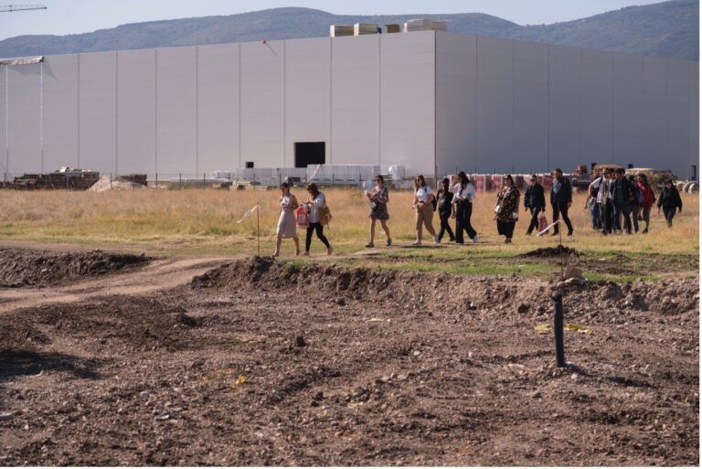 People walking on grass in front of a factory building. Biodiversity mapping of Kuklen Industrial Park with Municipality of Kuklen in the framework of the scientific exchange project New Ruralities Photo: Sandro Arabyan