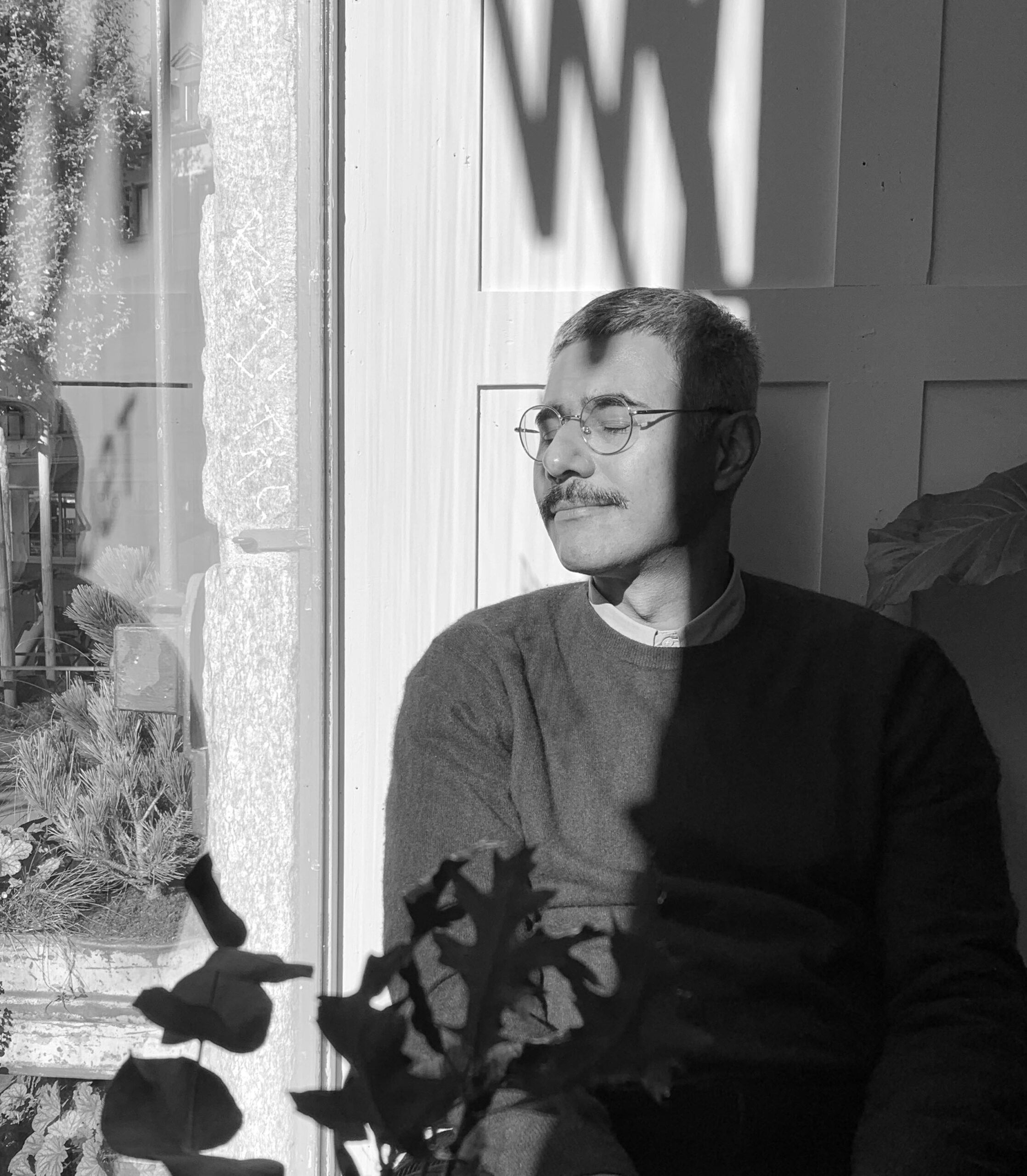 Portrait of Nitin Bathla, black and white, with closed eyes outside, in front of a house door.
